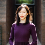 Xi Song, standing outside, posing in front of a door frame entrance to a building. 